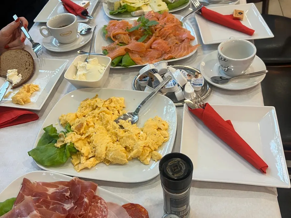 Gedeckter Frühstückstisch mit Rührei, Lachs, Aufschnitt, Käse und Kaffeetassen, von oben