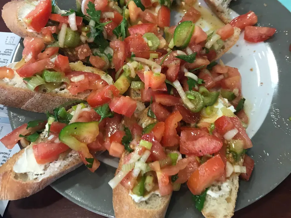 Vier Scheiben Bruschetta mit gewürfelten Tomaten, Gurke, Zwiebeln und Kräutern