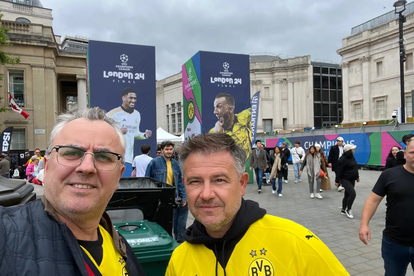 Zwei Fans in gelben Trikots auf dem Trafalgar Square, dahinter Banner zum Finale
