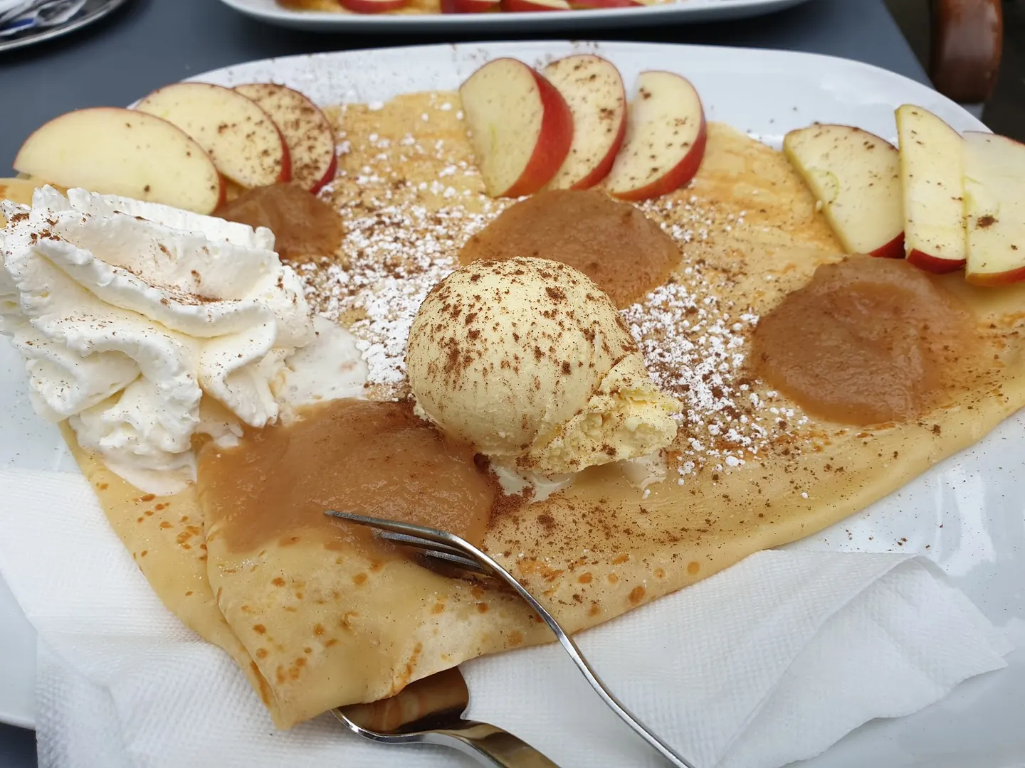 Apfelcrêpe mit Apfelscheiben, Zimt, Puderzucker, Vanilleeis und Sahne
