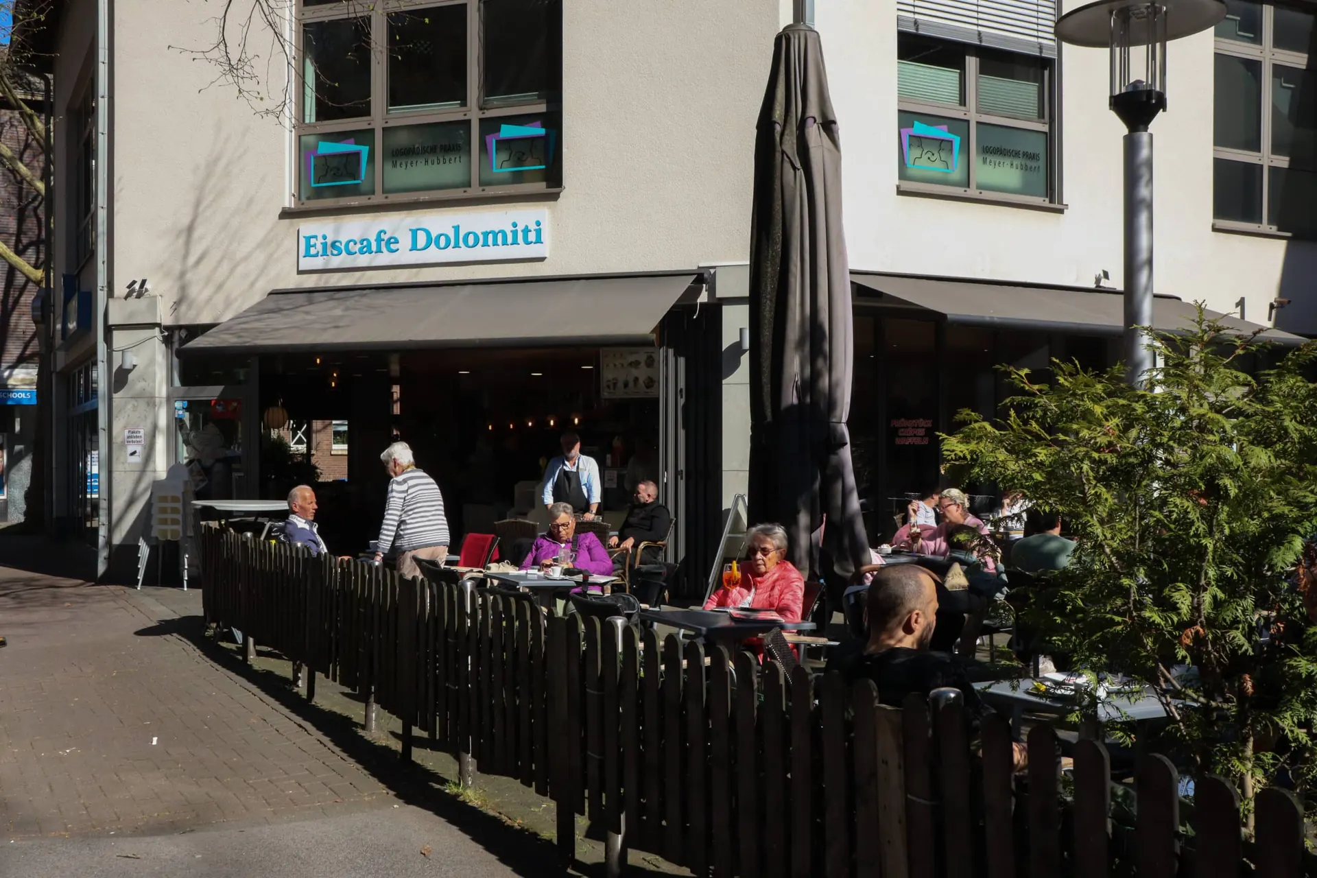Eiscafé Dolomiti am Mengeder Markt mit blauem Schriftzug, Markise und besetzter Terrasse