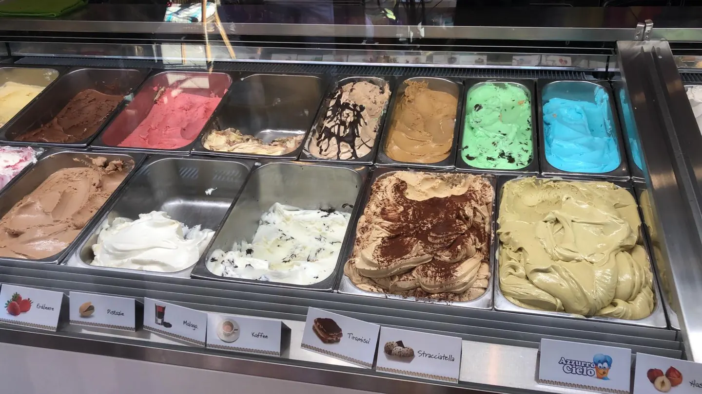 Eisvitrine mit beschrifteten Sorten wie Erdbeere, Pistazie, Malaga, Tiramisu und Azzurro Cielo