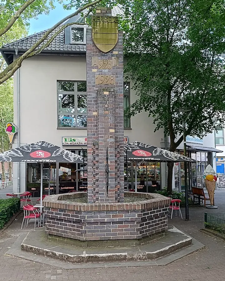 Brunnen von 1928 auf dem Mengeder Markt, dahinter die Sonnenschirme des Eiscafés