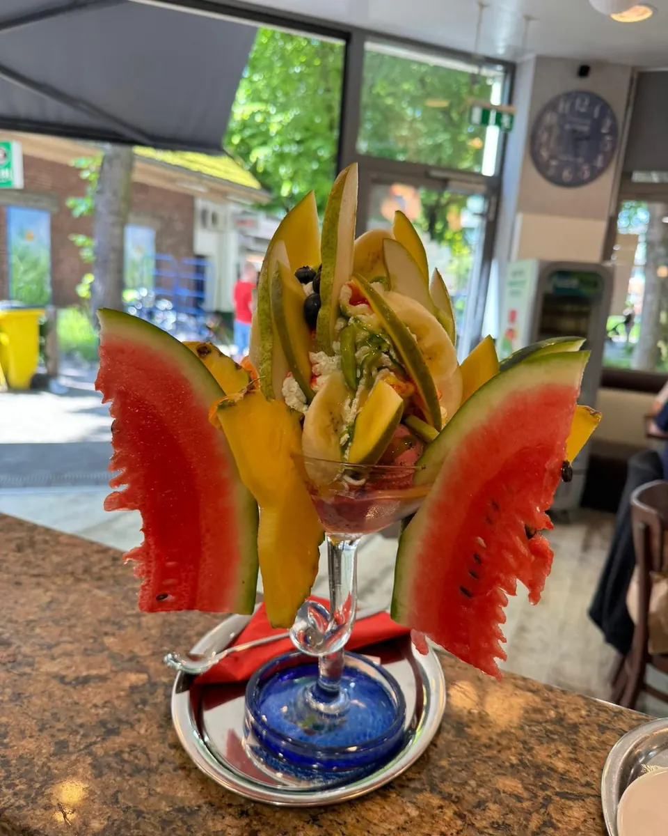 Hoher Fruchtbecher im Glas, besteckt mit Wassermelonen-, Melonen- und Mangoschnitten, auf der Theke am Fenster