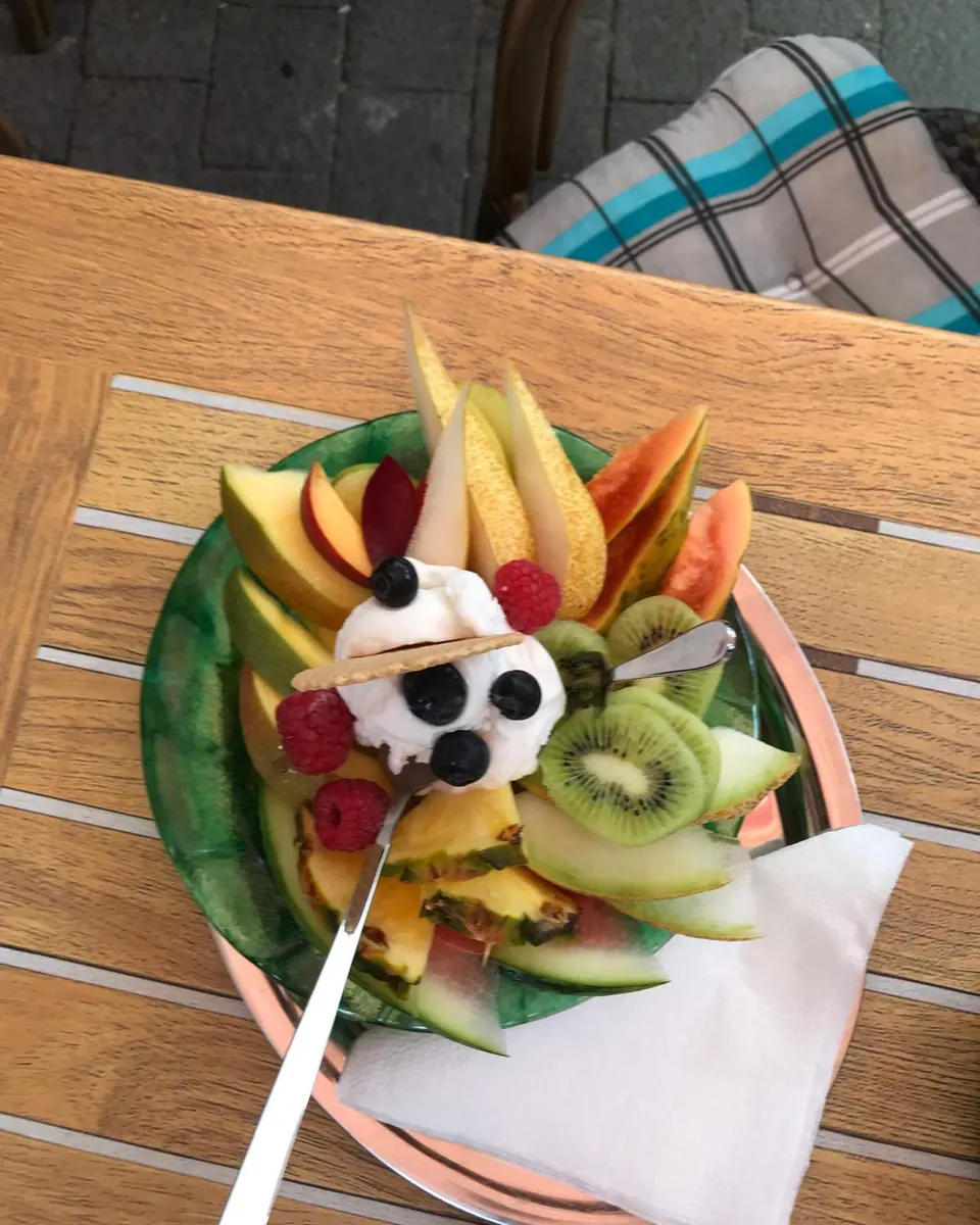 Fruchtteller mit Melone, Kiwi, Himbeeren und einer Kugel Eis auf dem Terrassentisch