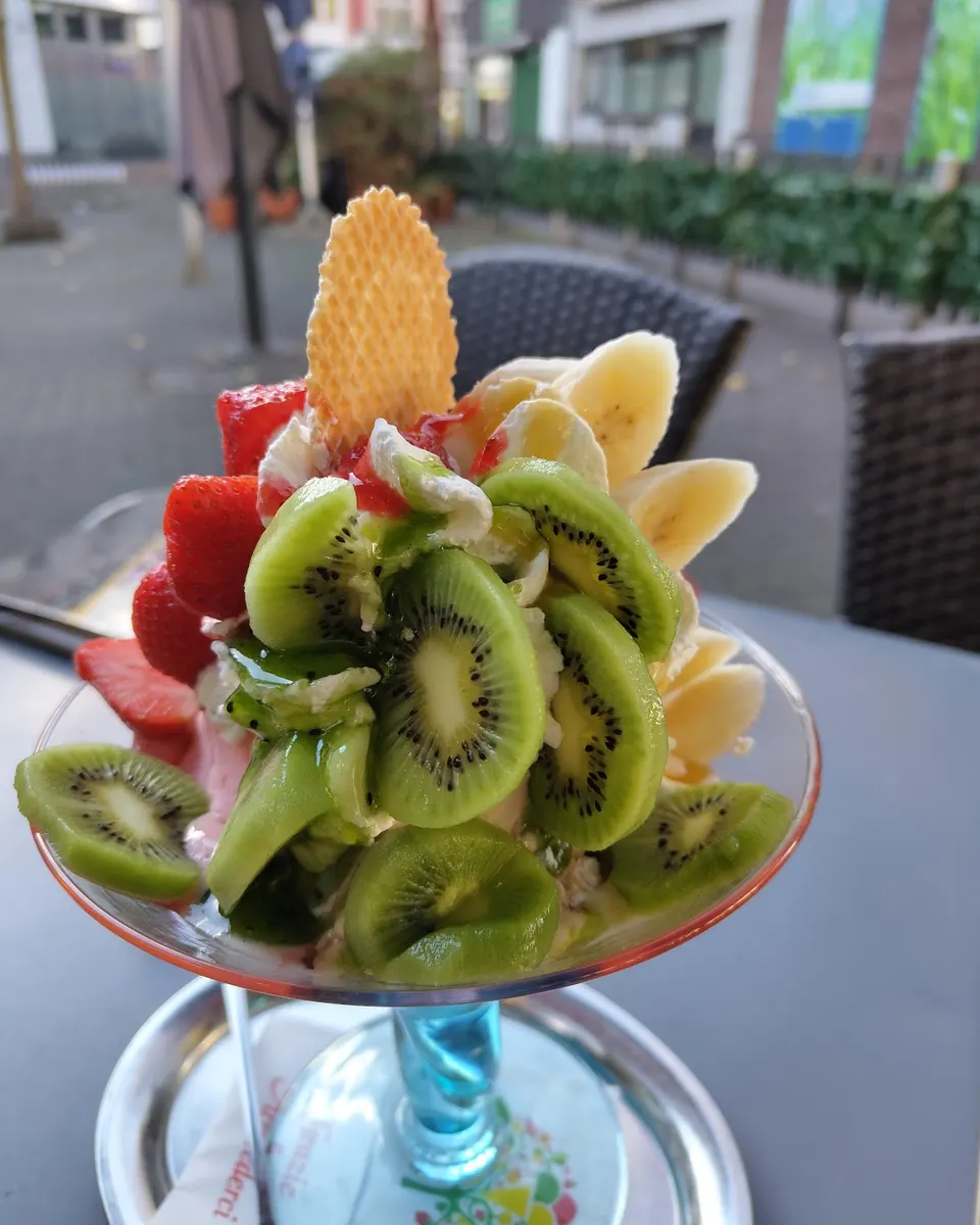Fruchtbecher mit Kiwi, Banane, Erdbeeren, Sahne und Waffel auf dem Terrassentisch