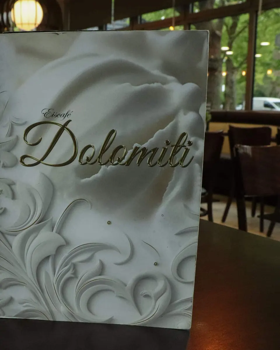 Speisekarte mit goldenem Dolomiti-Schriftzug neben einem Blumentopf auf dem Holztisch