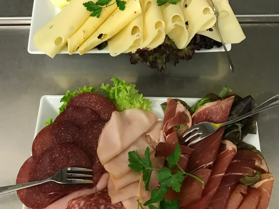 Käseplatte mit gerollten Scheiben, darunter eine Platte mit Salami, Kochschinken und Parmaschinken