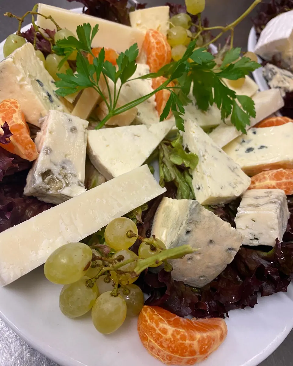 Käseplatte mit Brie, Blauschimmelkäse und Hartkäse auf Salat, dazu Trauben, Mandarinen und Petersilie