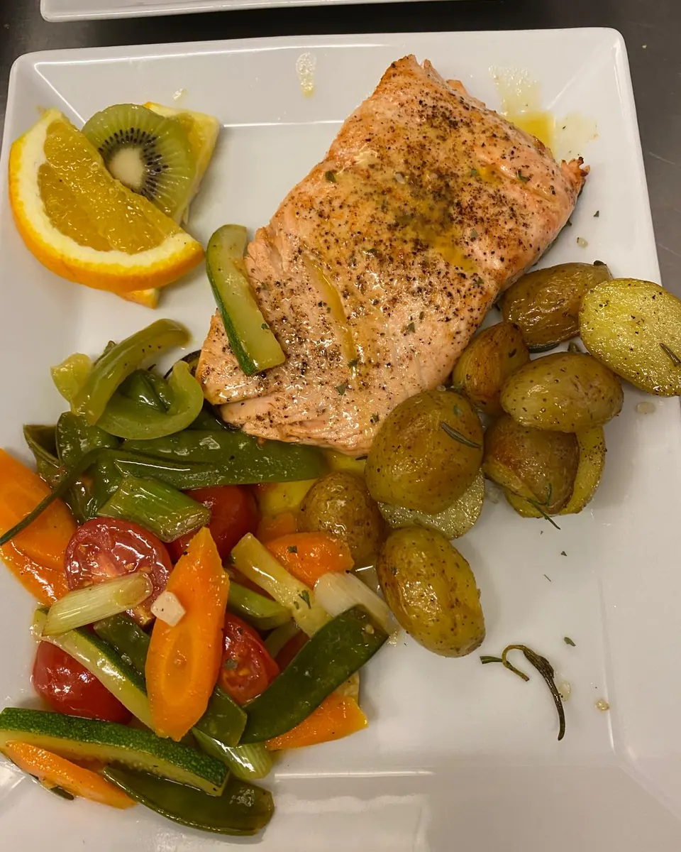 Teller mit Lachsfilet, Rosmarinkartoffeln und gebratenem Gemüse, dazu Orange und Kiwi