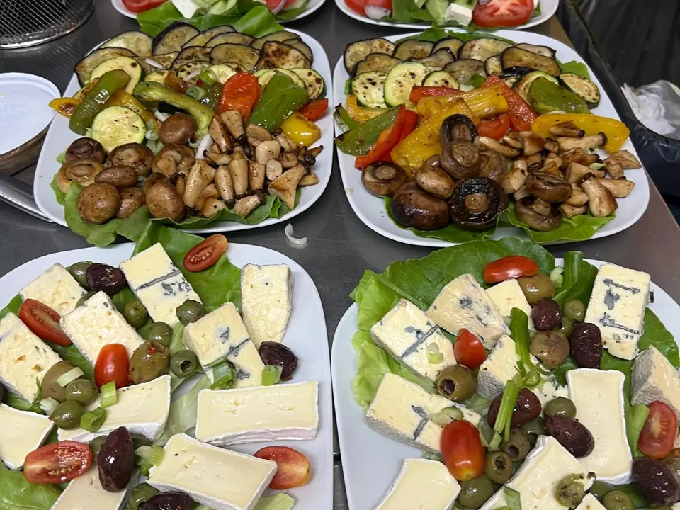 Mehrere Teller mit gegrilltem Gemüse, Champignons, Camembert, Oliven und Tomaten, für eine Feier vorbereitet
