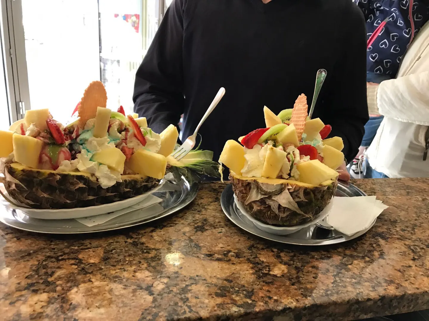 Zwei Ananasbecher in ausgehöhlten Ananashälften mit Sahne, Früchten und Waffel