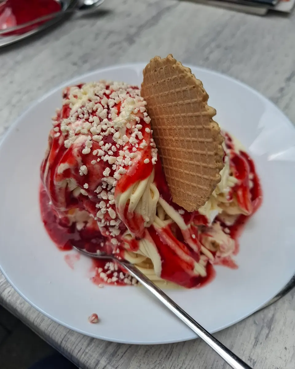 Klassisches Spaghettieis mit Erdbeersoße, weißen Schokoraspeln und Waffel