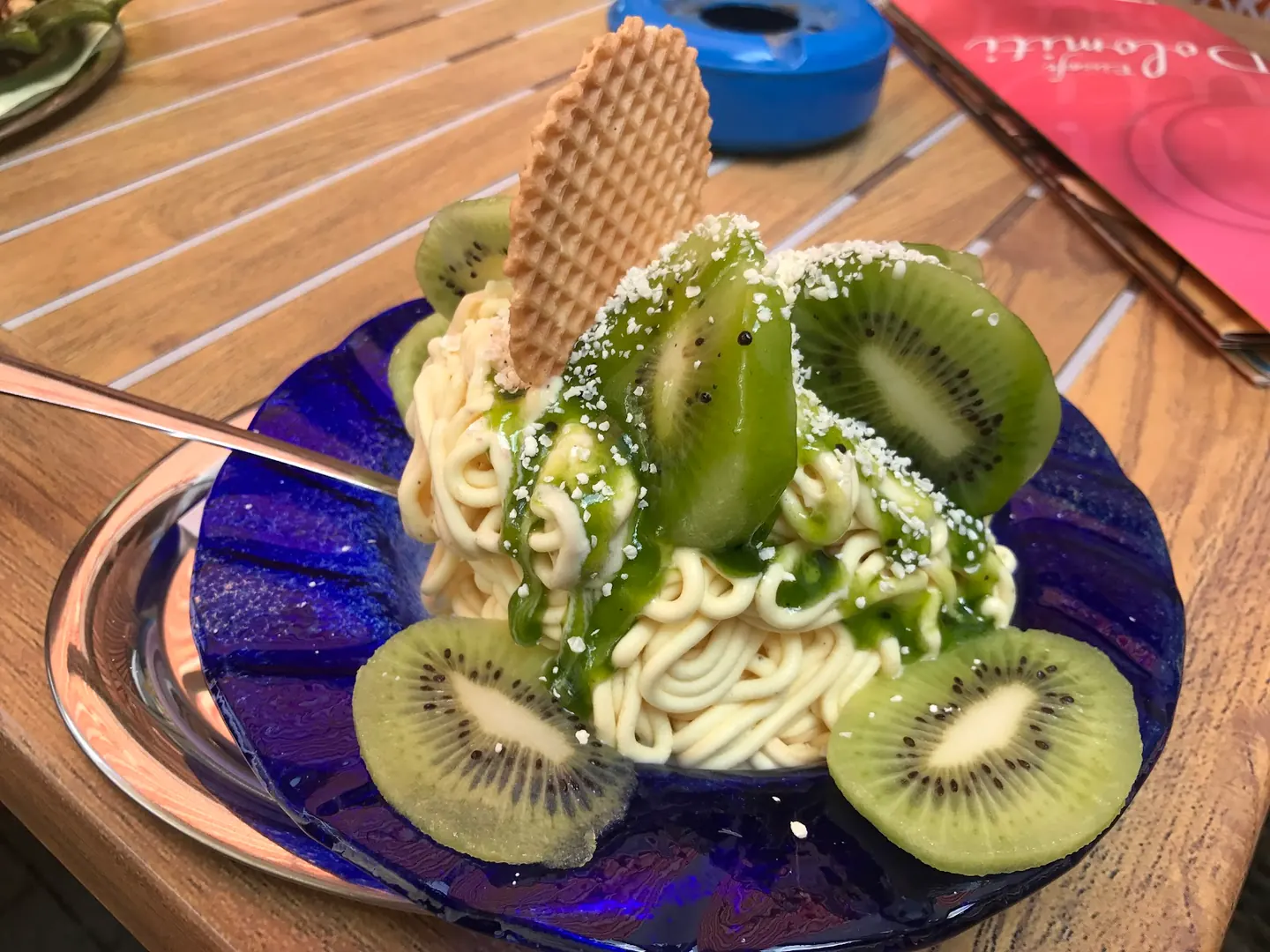 Spaghettieis mit Kiwisoße, frischen Kiwischeiben und Waffel auf blauem Glasteller