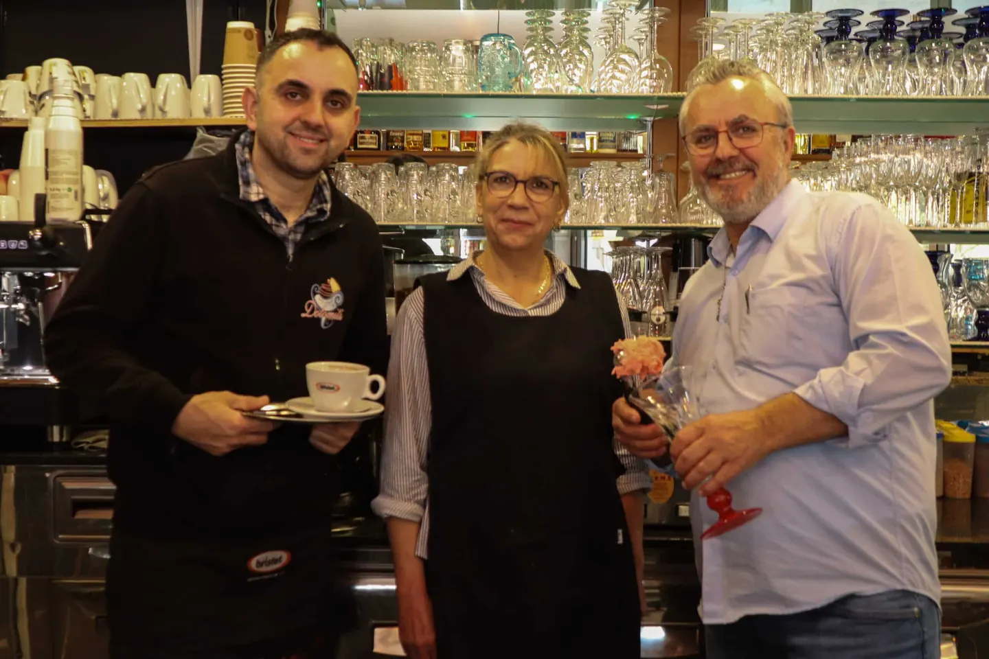 Drei Teammitglieder hinter der Bar, mit Cappuccino und Eisbecher in der Hand